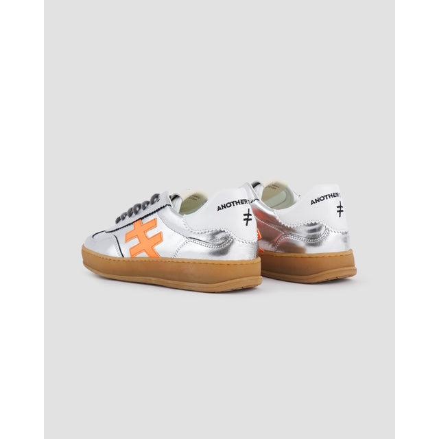 Metallic silver leather lace-up trainers with orange logo accents and tan rubber soles, trendy casual footwear for women.