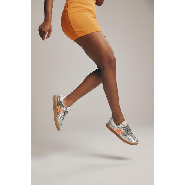 Metallic silver leather lace-up trainers with trendy design, worn by a model in an orange skirt, perfect for stylish activewear.