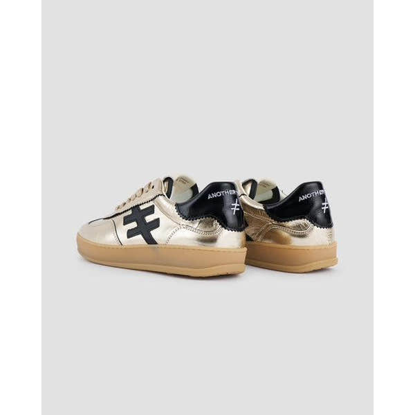 Gold metallic leather lace-up trainers with black and white accents, casual athletic style, from Trend Iconic Las Vegas collection.