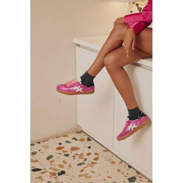 Pink fuchsia suede lace-up trainers with white logo details, styled with black socks and a pink outfit.