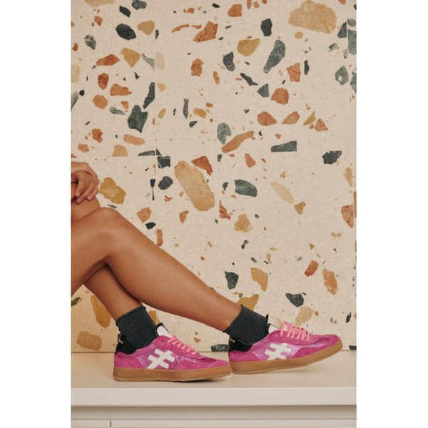 Pink suede lace-up trainers for women with white side logos, styled with black socks against a terrazzo background.