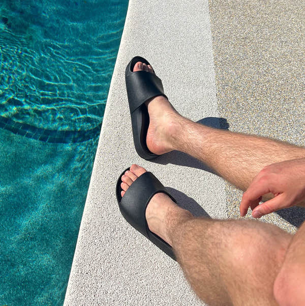 Unisex black waterproof Archies Arch Support Slides on a person's feet by a poolside. Classic slide sandals with arch support.