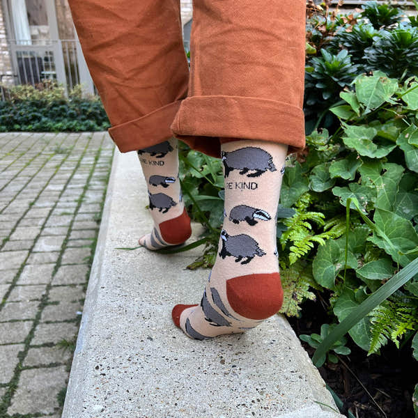 Barekind Save The Badgers bamboo socks featuring badger illustrations and the phrase "Be Kind," in beige, gray, and rust colors.