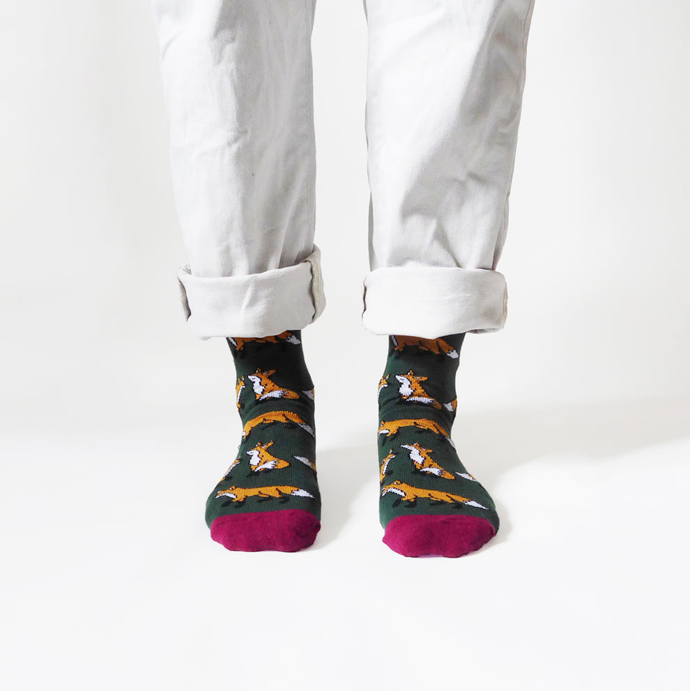 Barekind Save The Foxes Bamboo Socks with fox pattern, green base, and burgundy toes, displayed on person with rolled white jeans.