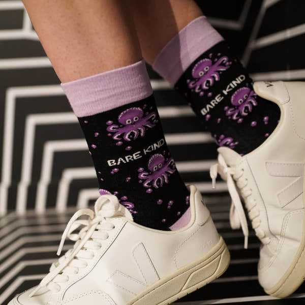 Barekind Save the Octopus bamboo socks featuring purple octopus design and "Bare Kind" text, paired with white sneakers.
