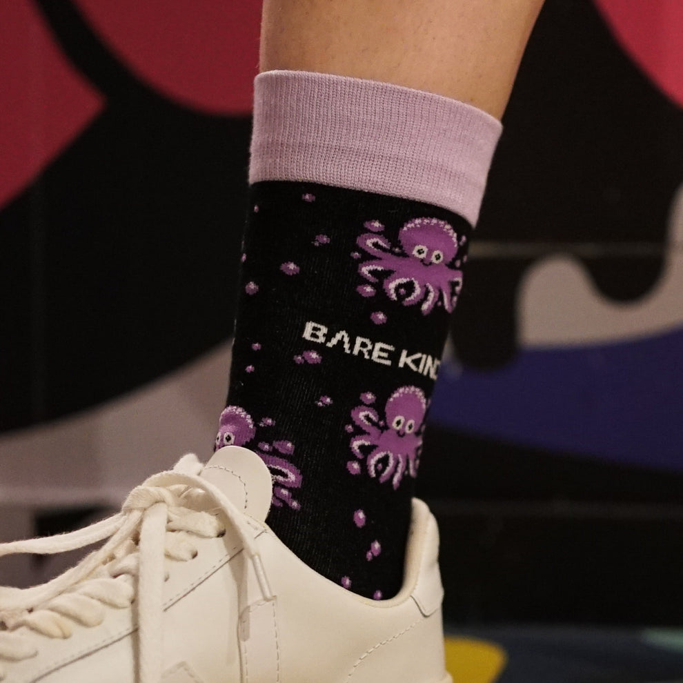 Barekind Save The Octopus black and purple socks with an octopus design, worn with white sneakers and light pink cuffs.