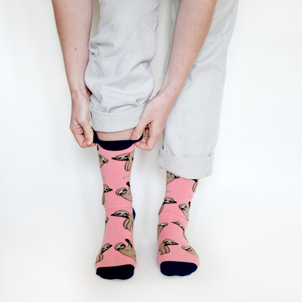 Barekind Save The Sloths pink socks with sloth pattern, navy toe and heel, worn with rolled light-colored pants.