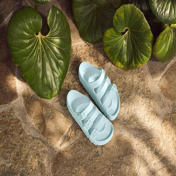Birkenstock Papillio Florida EVA III Flex platform sandals in surf green with buckle straps, on a stone surface surrounded by green leaves.