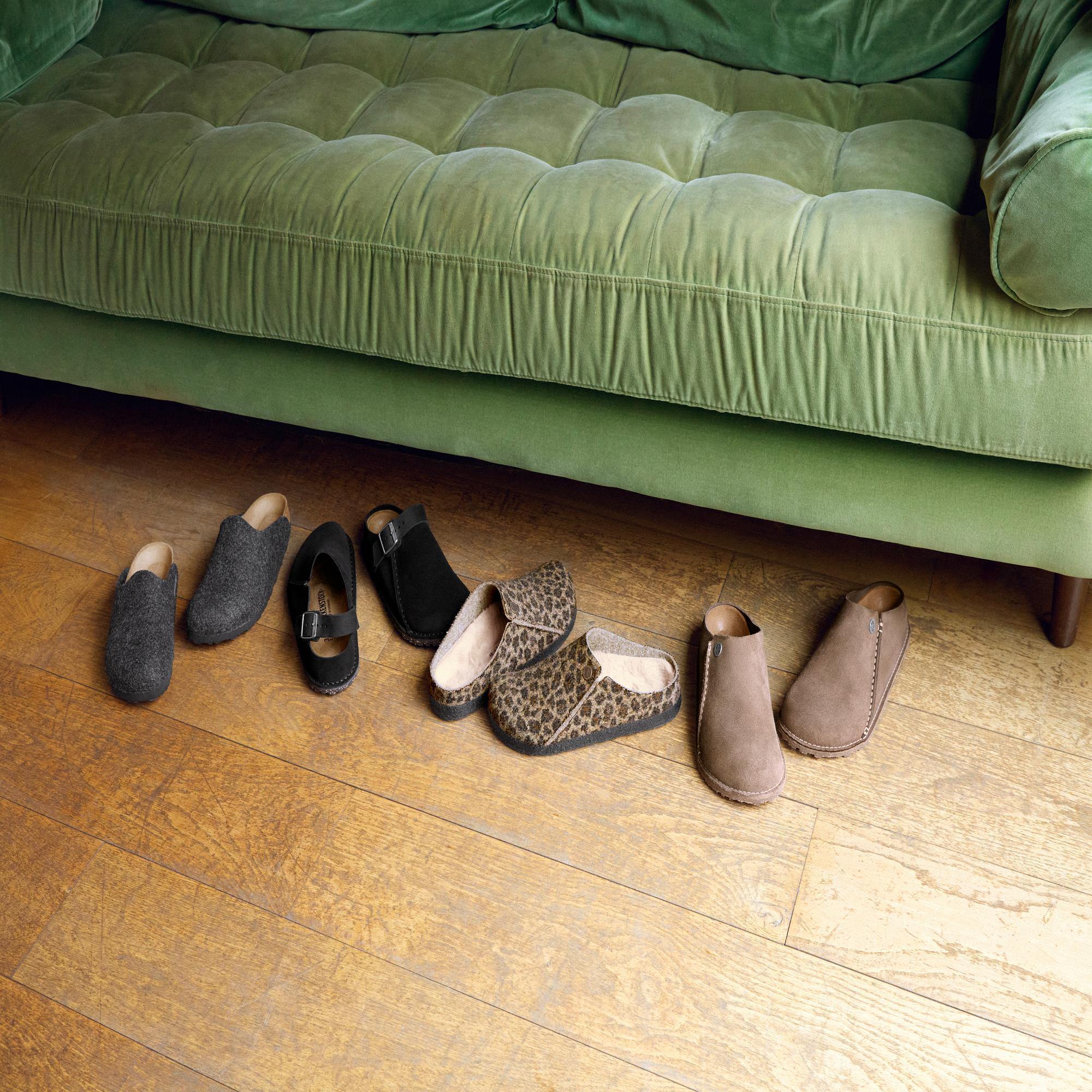 Birkenstock Zermatt Leopard shearling ladies slip-on slippers with textile upper and arch support, placed on wooden floor below green sofa.