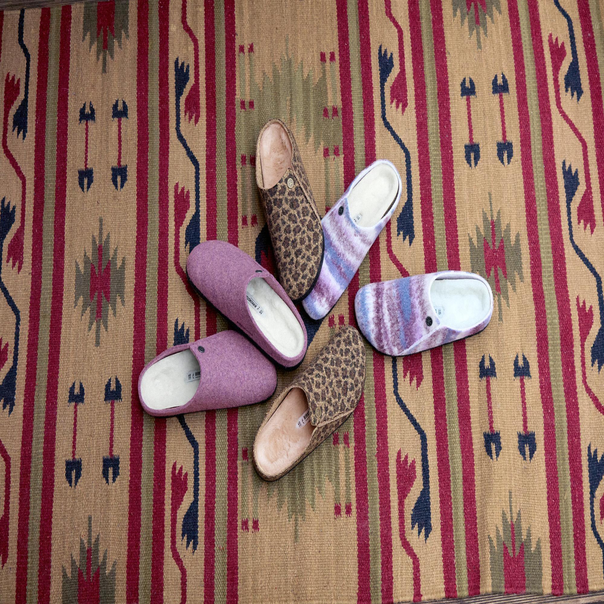 Pair of women's slip-on Birkenstock Zermatt mule slippers with leopard and colorful shearling patterns on a patterned rug.