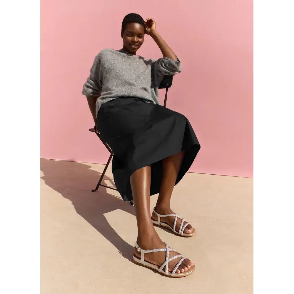 FitFlop Gracie Crystal ladies silver leather and textile sling back sandals worn by a woman sitting on a black chair against a pink background.