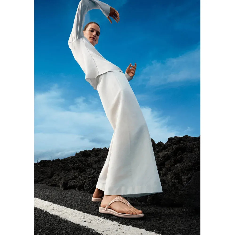 FitFlop Solay mixed-crystal nude rose T-strap sandals on a woman walking outdoors against a blue sky.