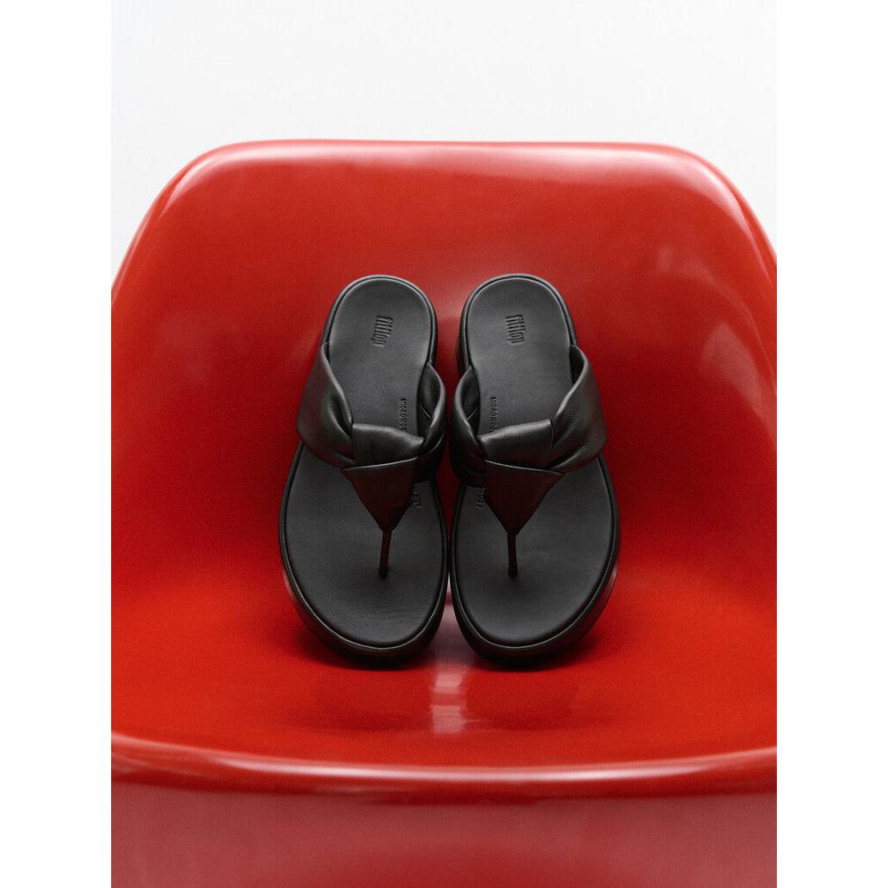 FitFlop IY1-090 F-Mode Knot women's black leather slip-on sandals on red chair. Stylish, comfortable footwear with knotted design.