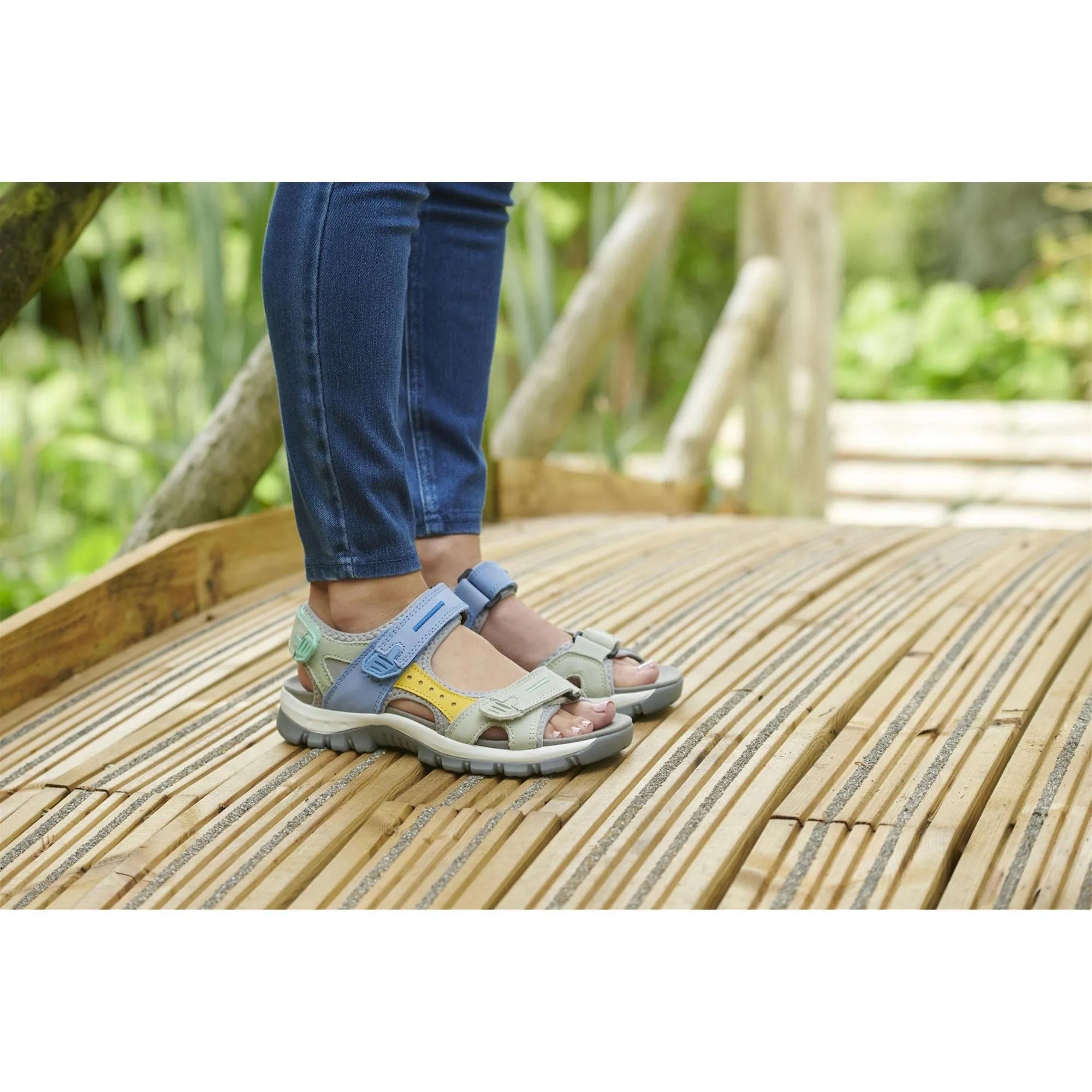 Josef Seibel Bella 10 ladies' blue leather and textile touch-fastening sandals on a wooden walkway, with adjustable straps.