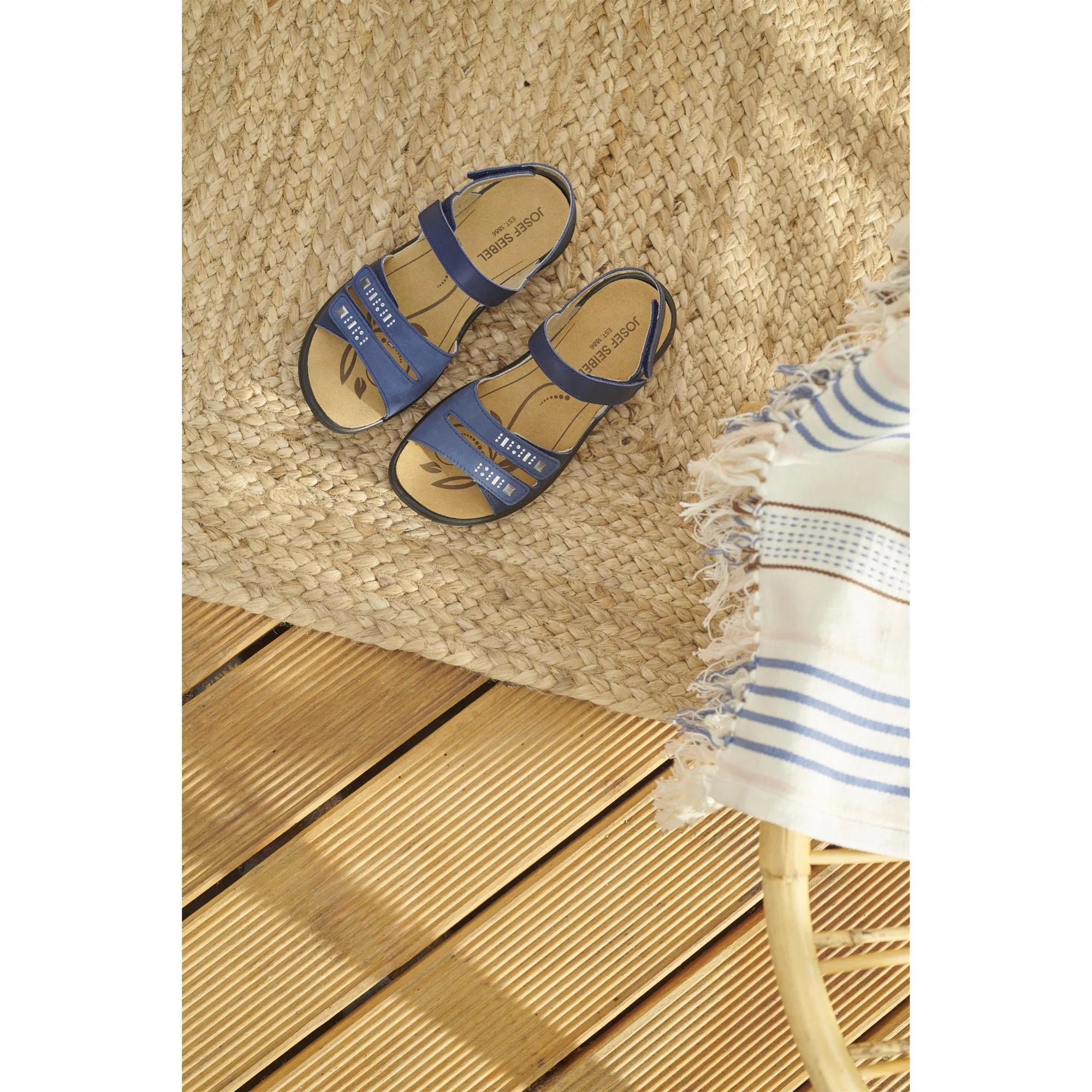 Josef Seibel Ibiza 86 women's ocean blue leather sandals with touch fastenings, on a woven straw mat with a striped cloth nearby.