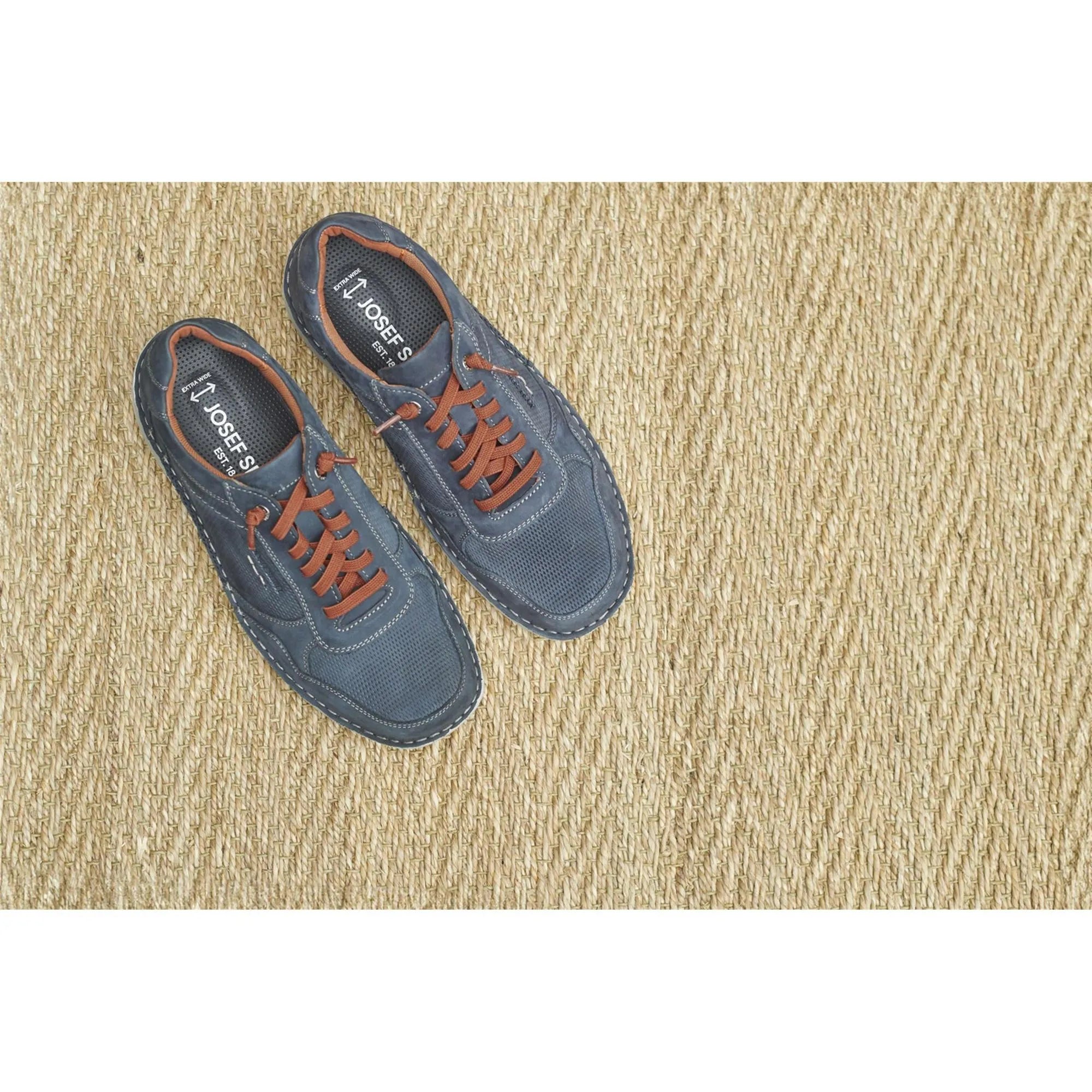 Men's navy blue leather lace-up shoes with orange laces, perforated toe and white stitching, on a woven beige rug.