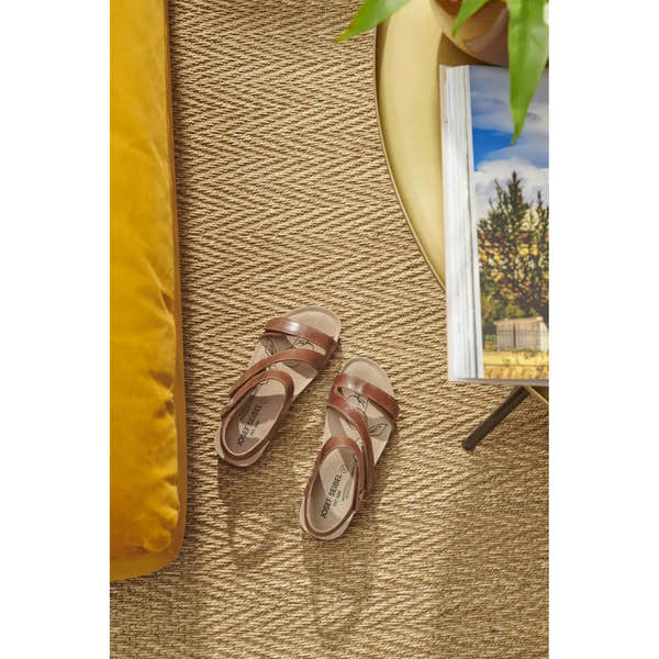 Josef Seibel Tonga 25 women's camel leather sandals on a woven rug, near a yellow table and open magazine.