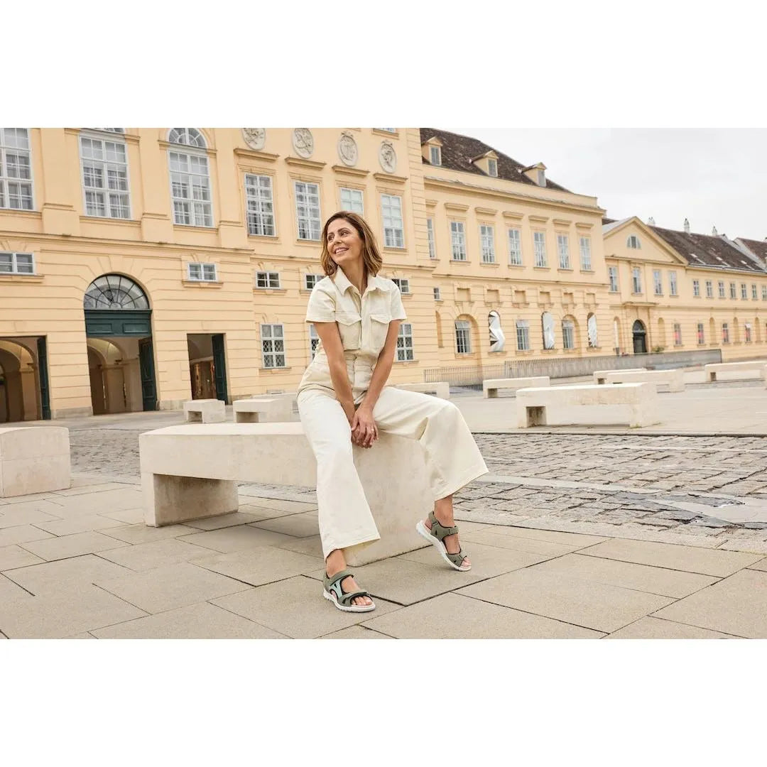 Women wearing beige wide-leg jumpsuit and Legero Siris Pino multi leather sandals outdoors in front of a historic yellow building.