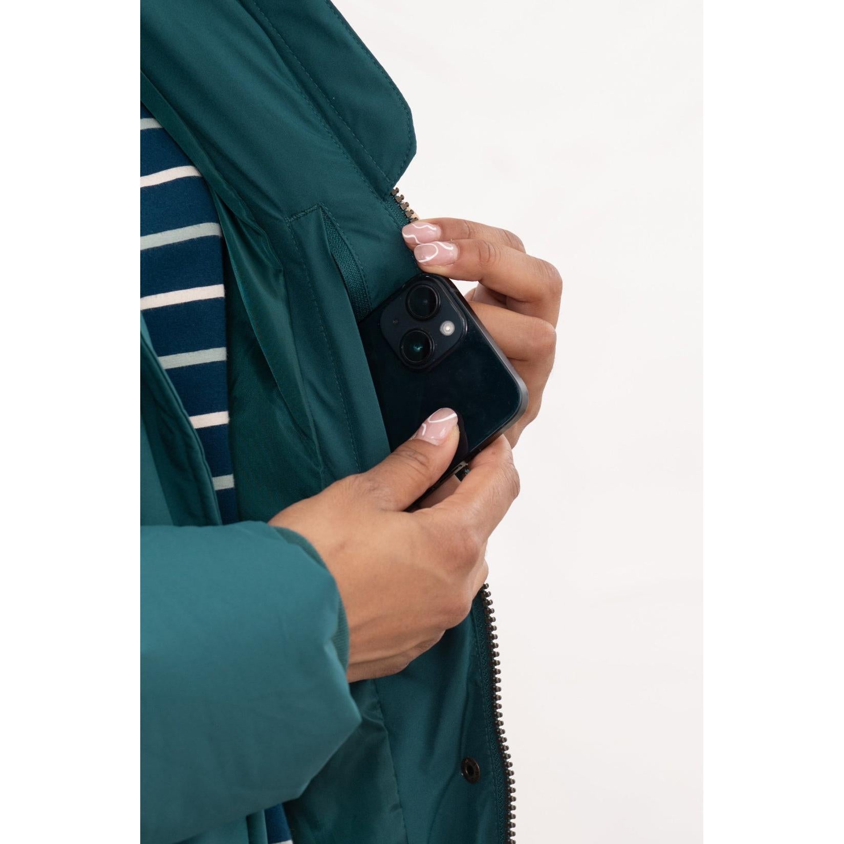 Lighthouse Savannah Pine Ladies Puffer Coat with front pocket, teal color, and striped shirt, holding a smartphone.