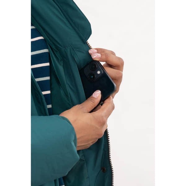 Lighthouse Savannah Pine Ladies Puffer Coat with front pocket, teal color, and striped shirt, holding a smartphone.