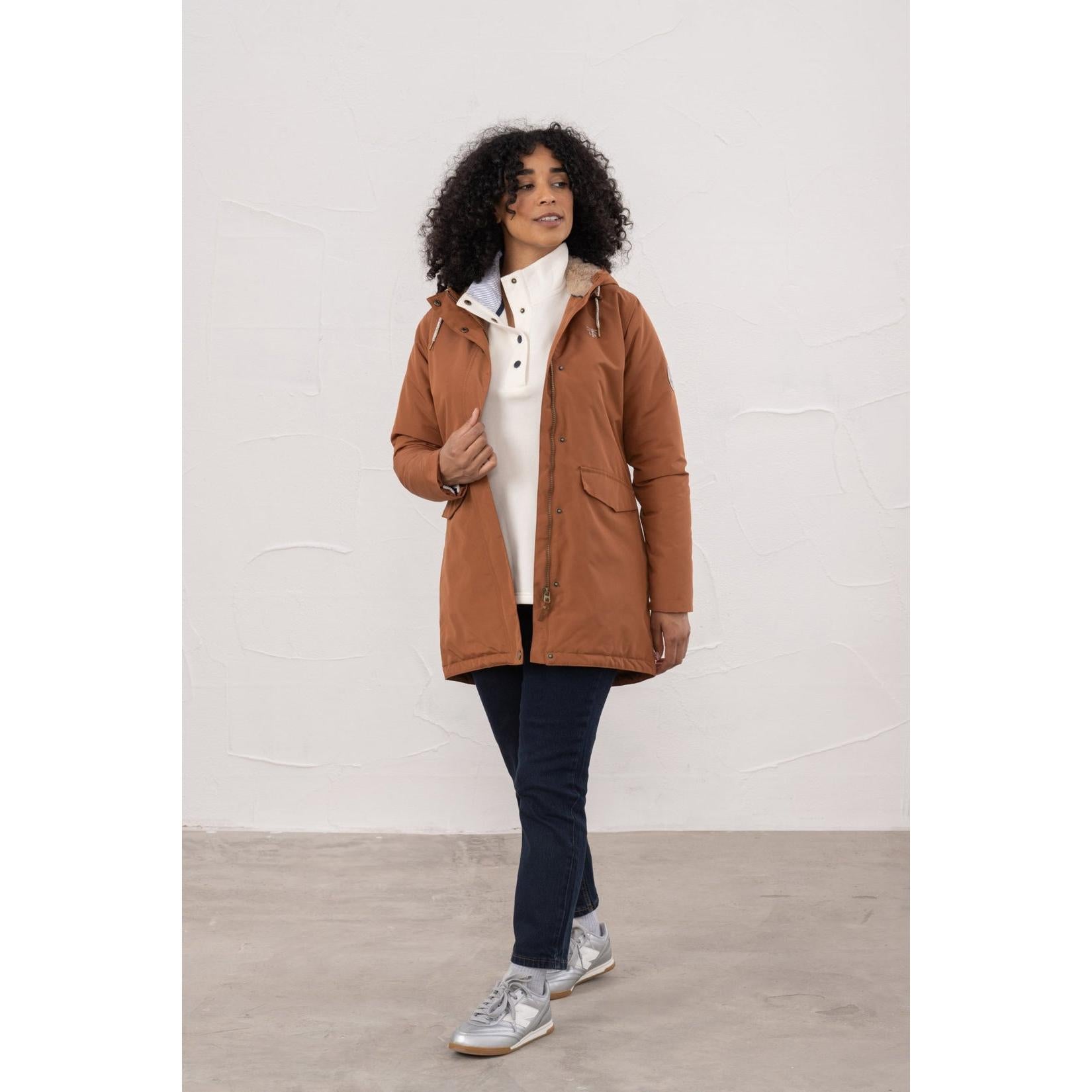 Lighthouse Scarlet Ladies Waterproof Coat in Rust color, with hood and front pockets, styled on a woman with dark jeans and sneakers.