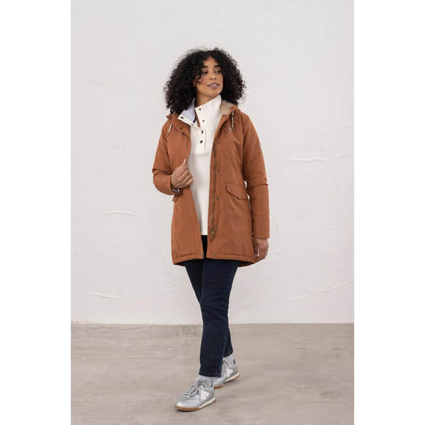 Lighthouse Scarlet Ladies Waterproof Coat in Rust color, with hood and front pockets, styled on a woman with dark jeans and sneakers.