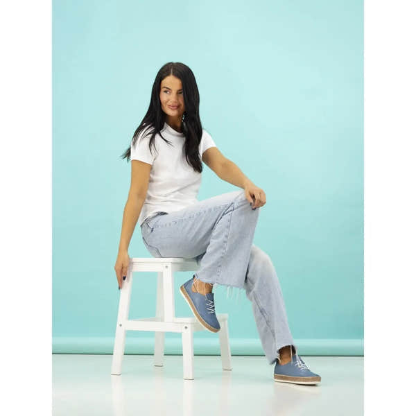 Lunar FLE050 Evie Ladies Mid Blue Leather Elasticated Shoes displayed on a woman sitting on a white stool against a light blue background.