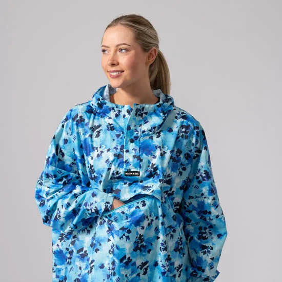 Unisex festival poncho in blue daze with floral print, hood, pocket, and half-zip design, ideal for outdoor events and rain protection.
