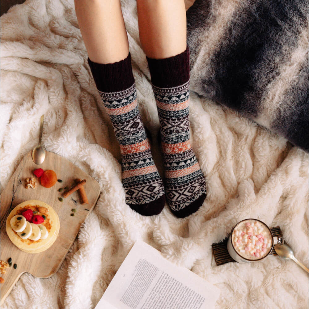 Unisex brown wool Nordic socks with festive snowflake patterns, worn by a person sitting on a cozy blanket.