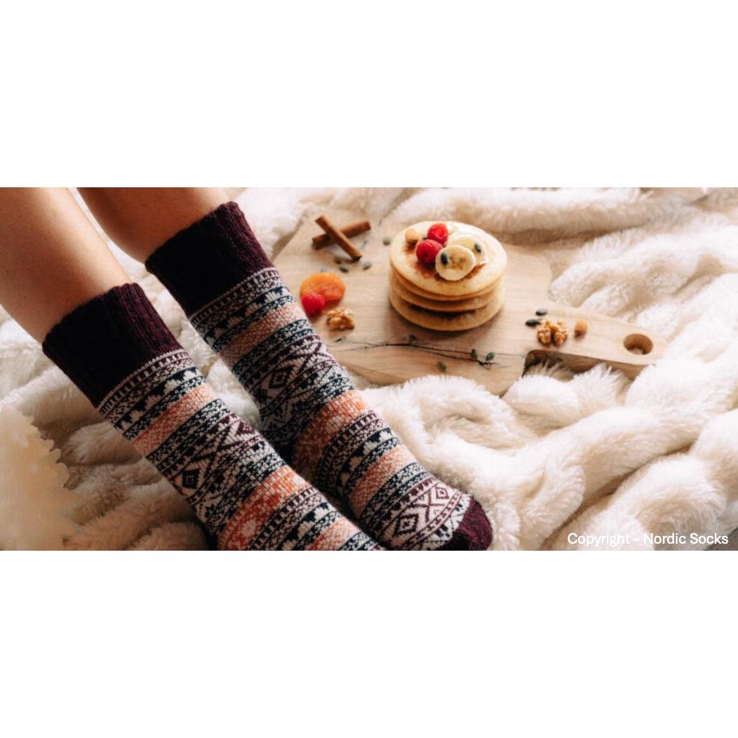 Unisex Nordic socks in burgundy with geometric patterns, worn by someone sitting on a cozy white fur blanket, with pancakes and fruit nearby.