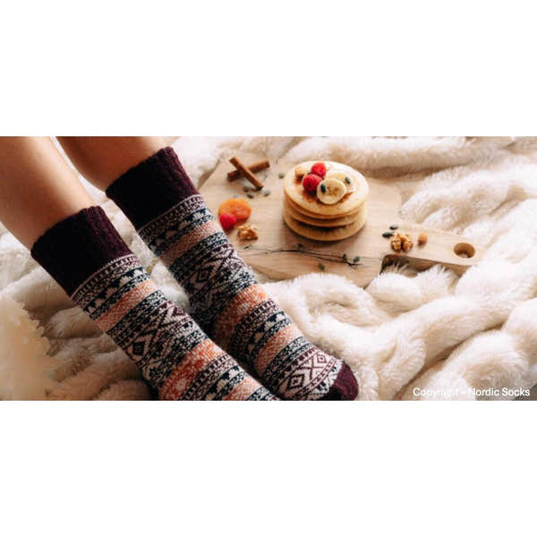Unisex Nordic socks in burgundy with geometric patterns, worn by someone sitting on a cozy white fur blanket, with pancakes and fruit nearby.