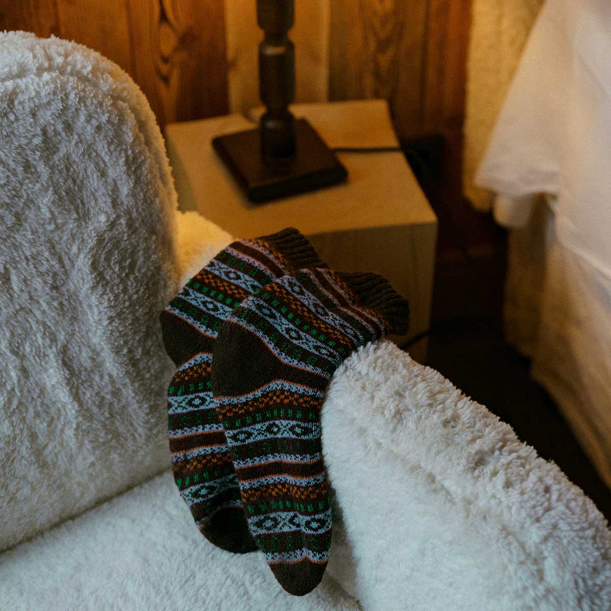 Nordic unisex Arvid wool socks in red with colorful Nordic patterns, displayed on a cozy cream chair.
