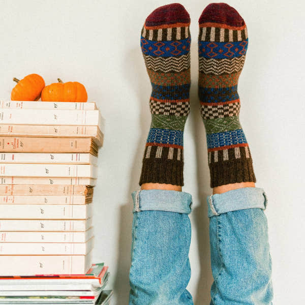 Unisex Nordic wool socks in brown with colorful geometric patterns, worn with rolled-up jeans, in a cozy fall setting.