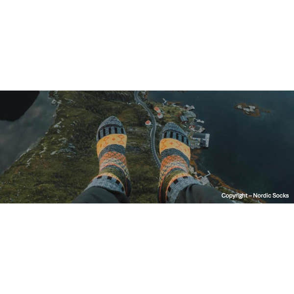 Unisex Nordic Socks Svea Wool Grey worn outdoors, featuring colorful Nordic patterns, in a landscape over water and countryside.