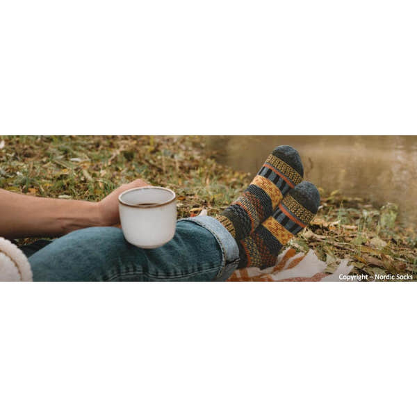 Unisex Nordic Socks Svea Wool Grey with geometric patterns, worn by person relaxing outdoors with a cup of coffee on autumn leaves.