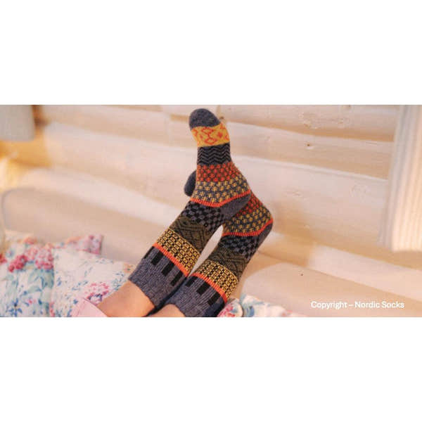 Unisex grey wool Nordic Socks Svea, featuring colorful geometric and traditional Scandinavian patterns, worn by a person lying on a bed.