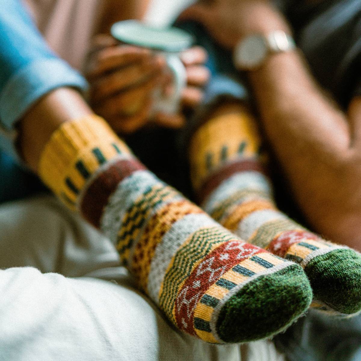 Unisex Nordic wool socks in yellow with colorful Nordic patterns, worn by a person holding a smartphone.