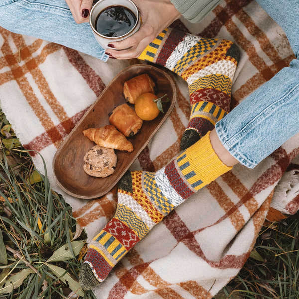 Unisex Svea Wool Nordic Socks in vibrant yellow with traditional Scandinavian patterns, worn with jeans during a cozy outdoor picnic.