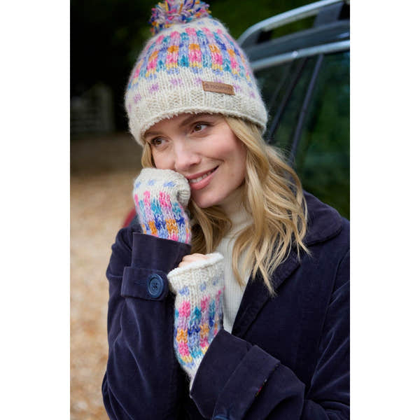 Woman wearing an oatmeal-colored Pachamama Arundel bobble beanie and multicolored knit mittens outdoors.