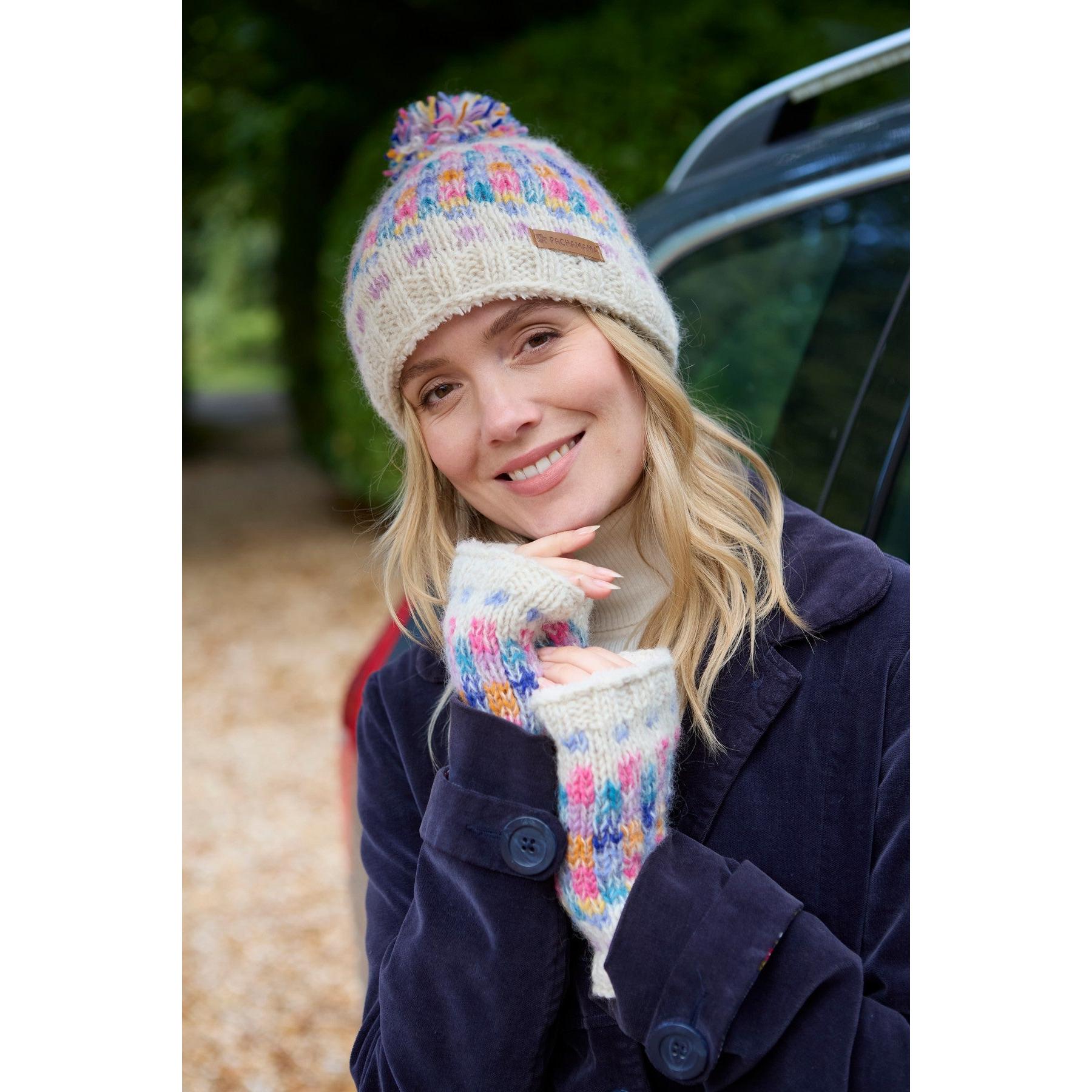 Pachamama Arundel Bobble Beanie in oatmeal with colorful knit pattern and pom-pom, worn by smiling woman outdoors, autumn setting.