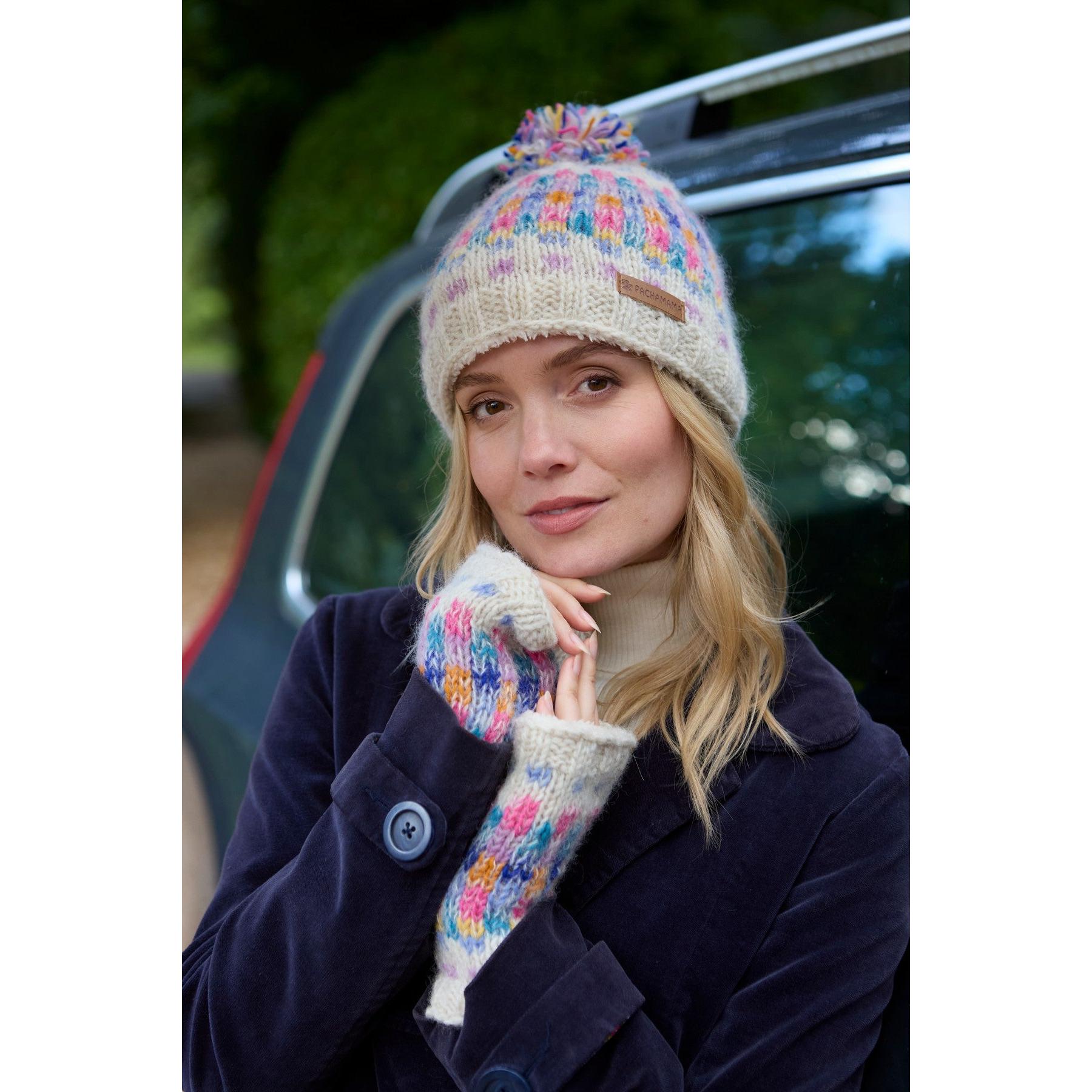 Pachamama Arundel Bobble Beanie in oatmeal yarn with colorful patterns and pom, worn by woman outdoors, cozy winter accessory.