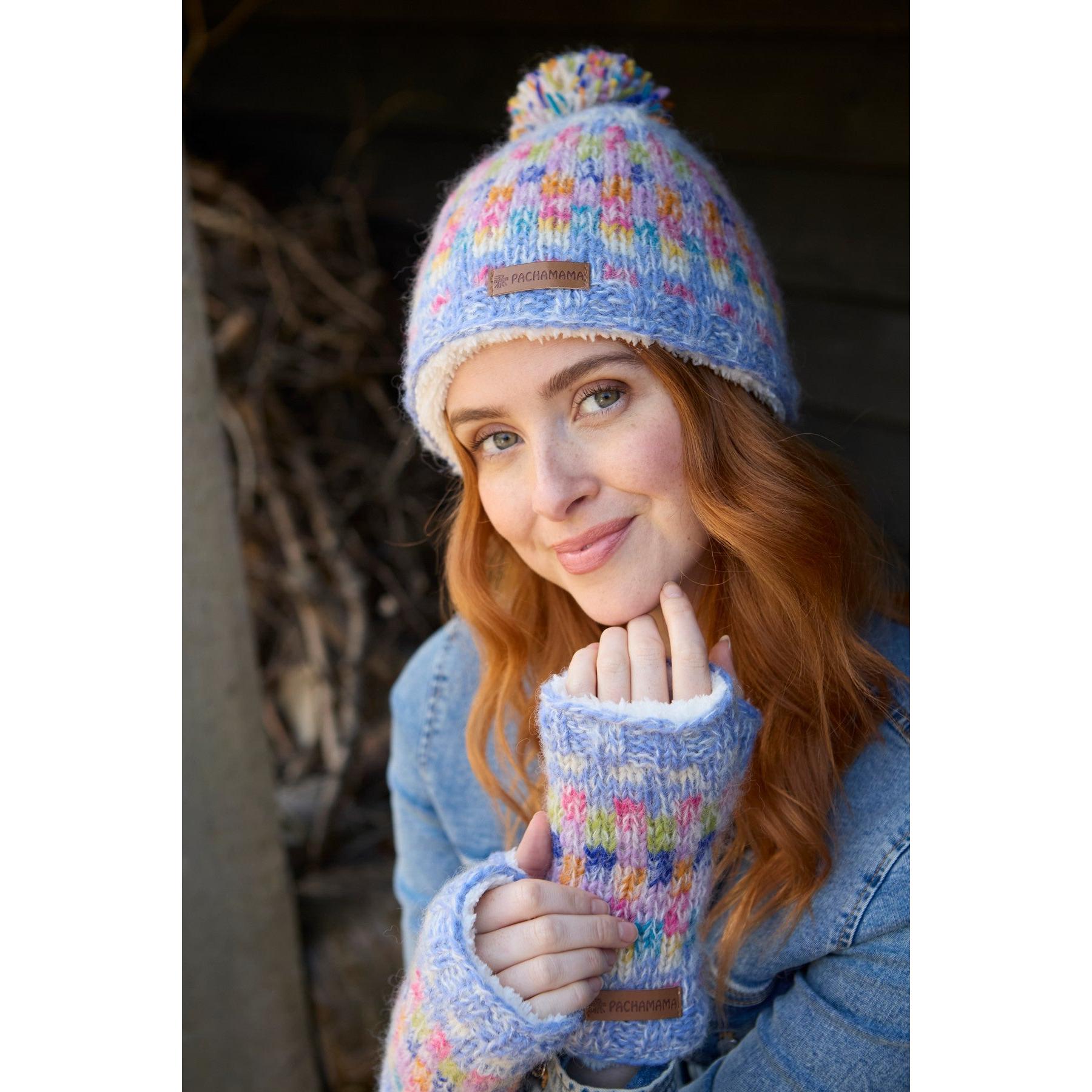 Pachamama Arundel Bobble Beanie Sky with colorful knit pattern, pom-pom, and cozy fingerless gloves, worn by smiling woman outdoors.