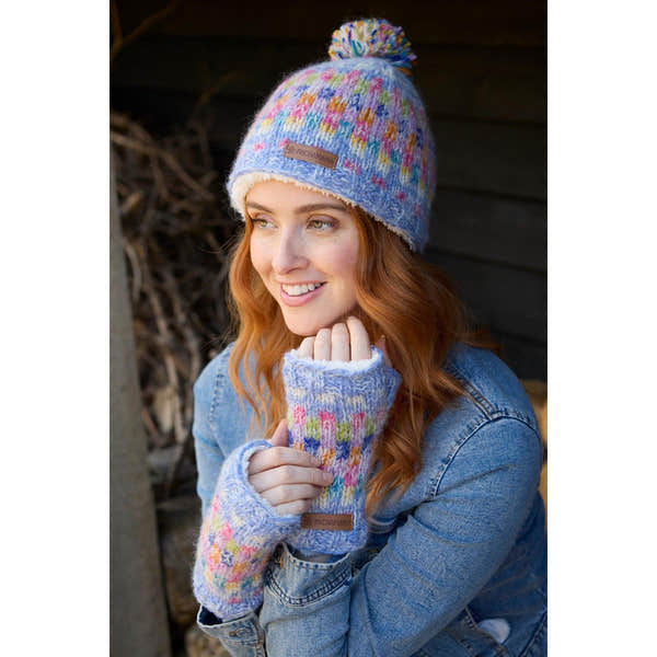 Pachamama Arundel Sky bobble beanie and colorful knit fingerless gloves on smiling woman outdoors.