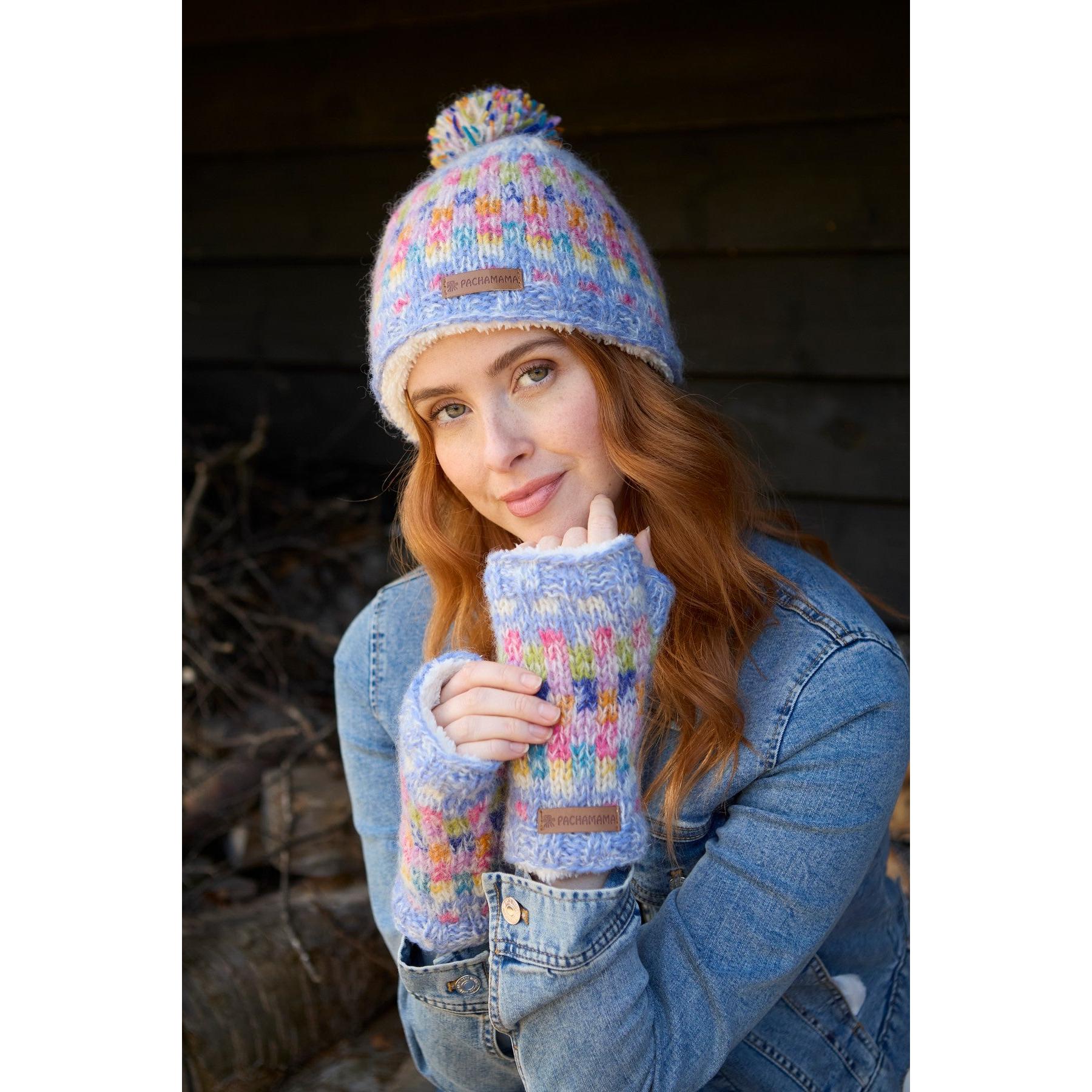 Woman wearing a colorful Pachamama Arundel Bobble Beanie and matching fingerless gloves, outdoors, casual denim jacket.