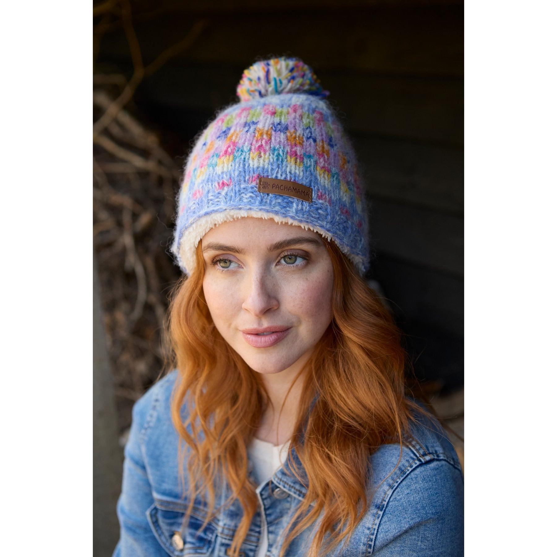Pachamama Arundel Bobble Beanie Sky with multicolored knit pattern and pom-pom, worn by a young woman outdoors.