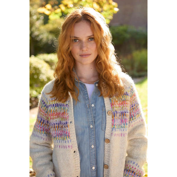 Woman wearing Pachamama Arundel Cardigan in oatmeal, cozy, chunky knit with colorful pattern, layered over denim shirt outdoors.