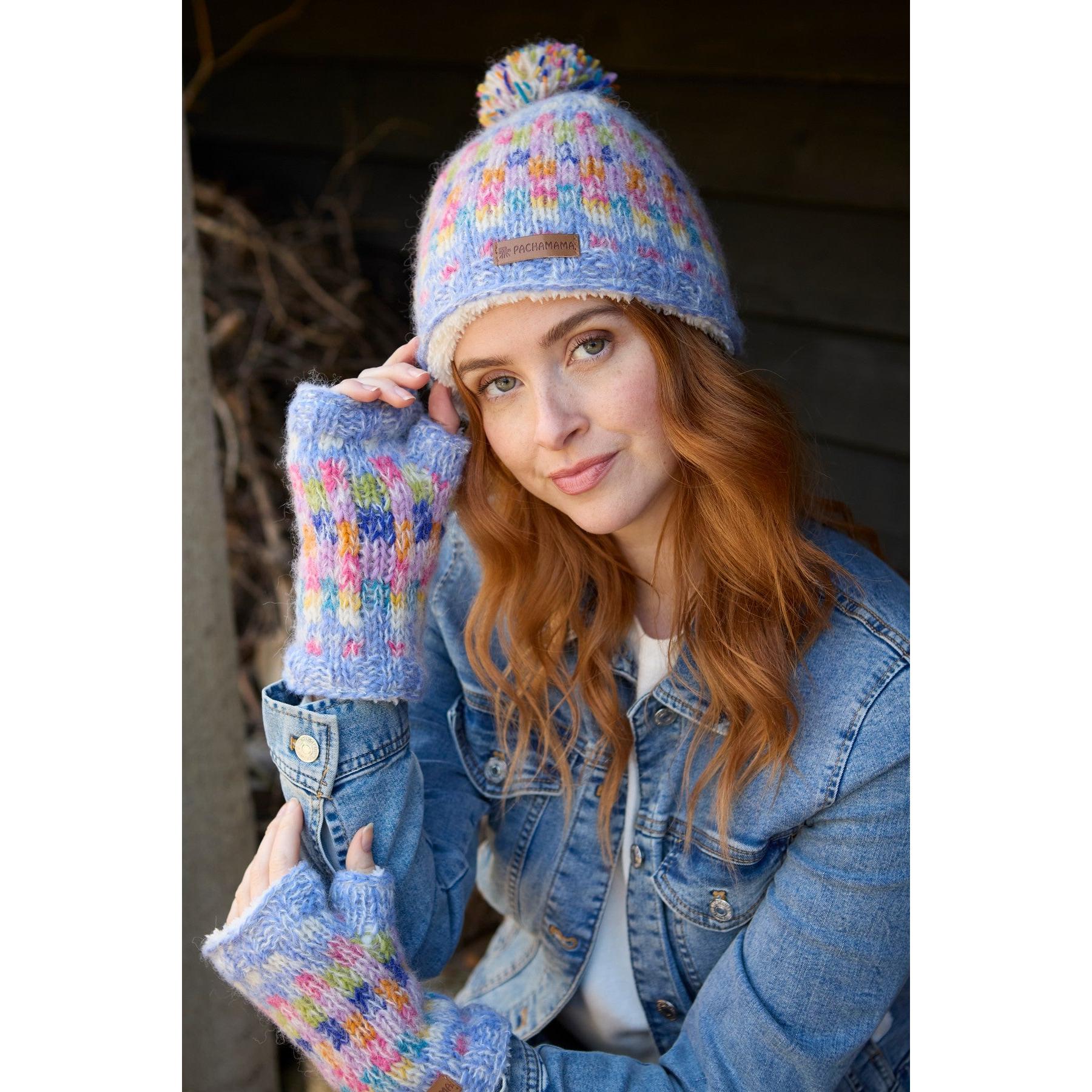 Woman wearing colorful knitted Pachamama Arundel Handwarmer Sky hat and mittens, denim jacket, outdoors.