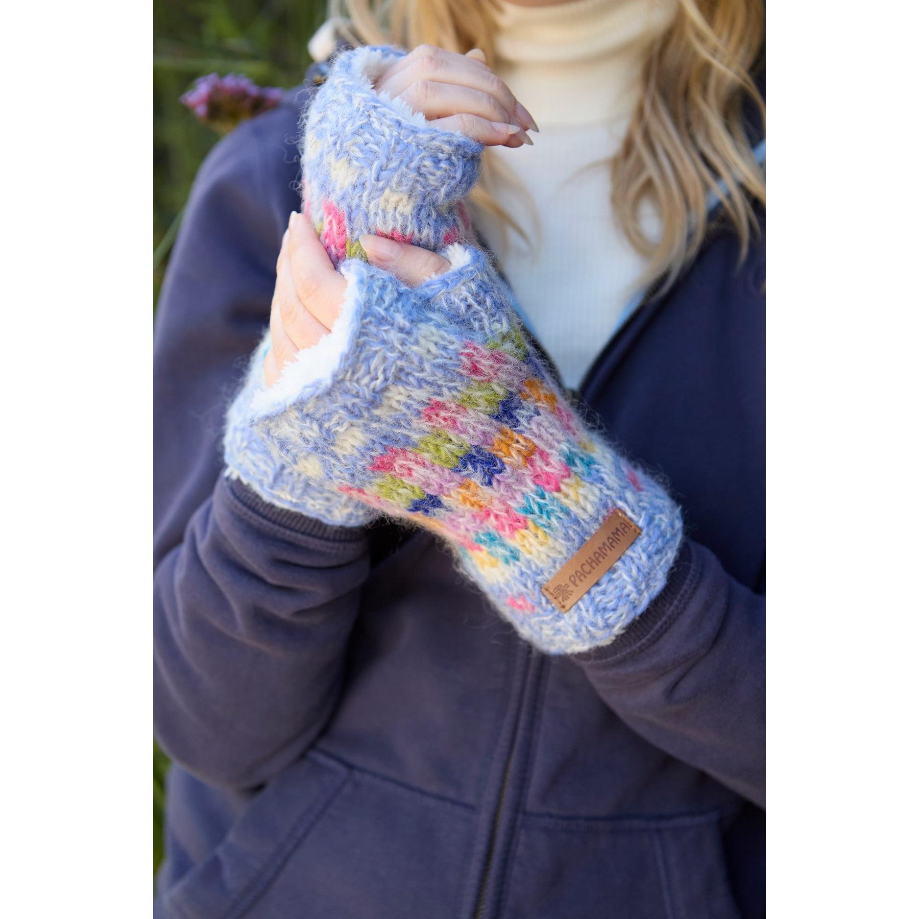Woman holding a colorful Pachamama Arundel Sky handwarmer with knitted floral design, fleece lining, and leather logo patch.