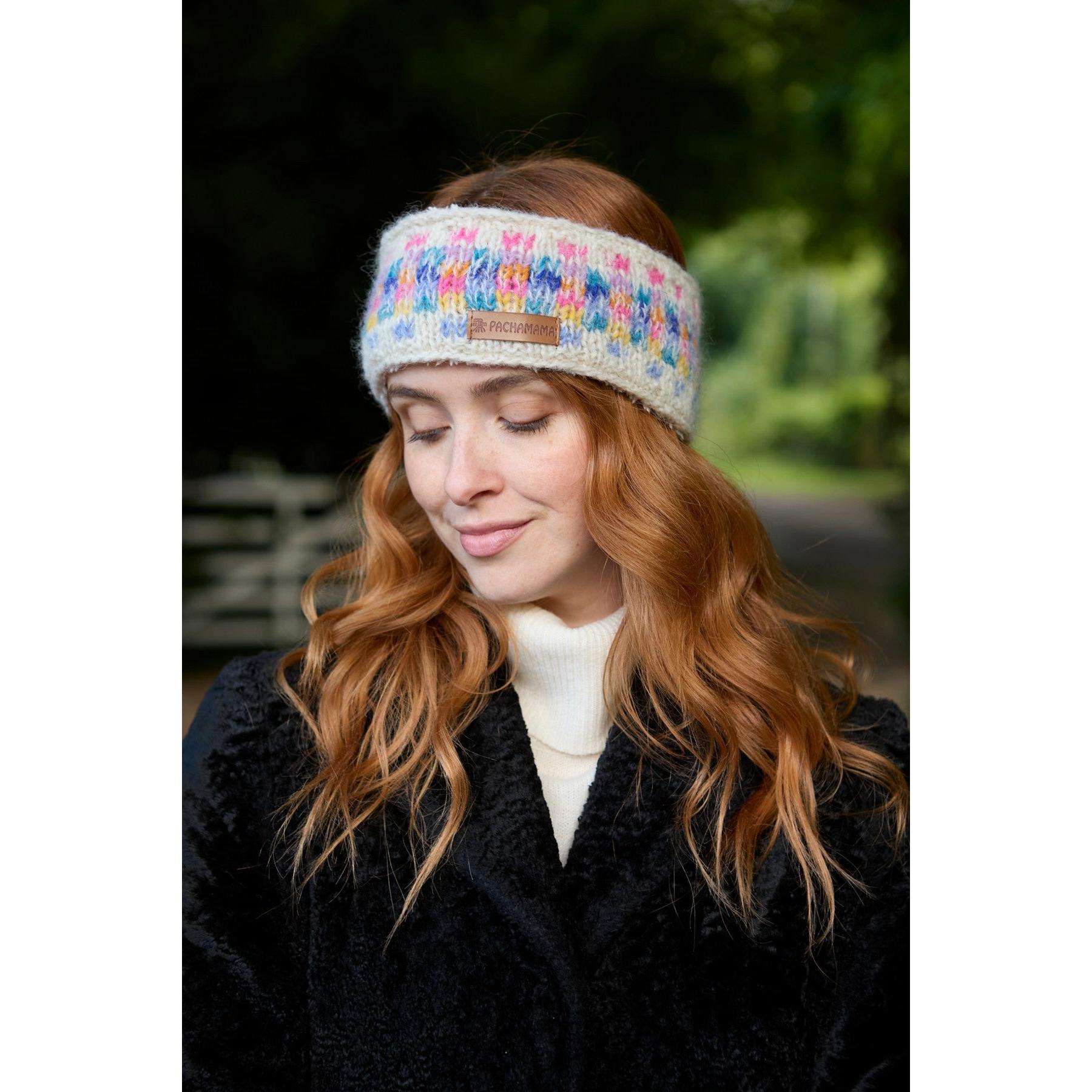 Woman wearing an oatmeal-colored Pachamama Arundel headband with colorful woven design, outdoors with green foliage background.