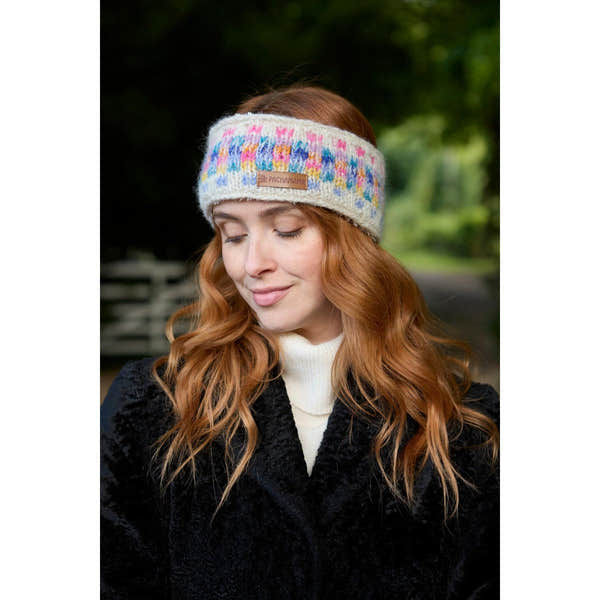 Woman wearing an oatmeal-colored Pachamama Arundel headband with colorful woven design, outdoors with green foliage background.
